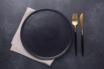 Empty ceramic plate, linen napkin and cutlery on dark stone background Copy space Top view