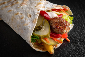 A delicious doner donair kebab wrap with meat, lettuce, tomato, red onion and sauce.