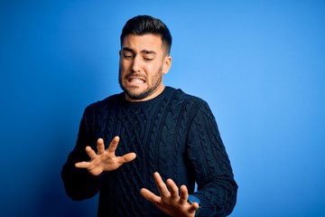 Young handsome man wearing casual sweater standing over isolated blue background disgusted...