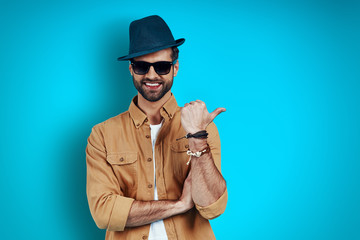 Charming young man smiling and pointing copy space while standing against blue background