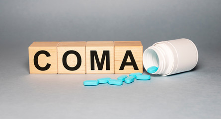 Coma - word from wooden blocks with letters on grey background with a jar of pills