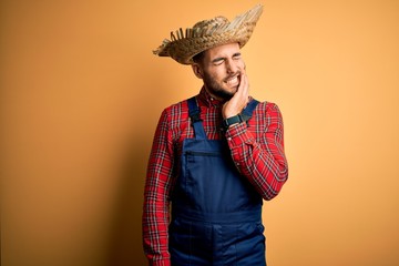 Young rural farmer man wearing bib overall and countryside hat over yellow background touching...