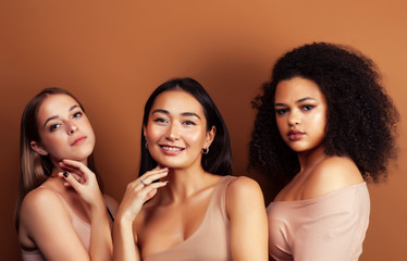 young pretty asian, caucasian, afro woman posing cheerful together on brown background, lifestyle diverse nationality people concept