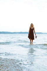 Obraz premium woman in black light dress walking barefoot by sea beach