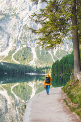 woman with backpack in yellow coat walking by path around lake at the morning