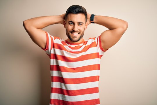 Young handsome man wearing casual striped t-shirt standing over isolated white background relaxing and stretching, arms and hands behind head and neck smiling happy