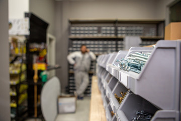 Focus on white metal screws in a plastic box. Behind is a man talking on the phone. Screws in a...