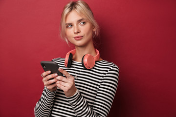 Image of nice thinking woman with headphones typing on cellphone