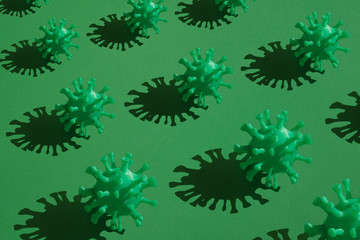 A set of green volumetric models of coronavirus with a hard shadow in rows on a green background. A conceptual pattern on the covid-19 theme..
