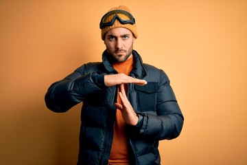 Young handsome skier man with beard wearing snow sportswear and ski goggles Doing time out gesture...