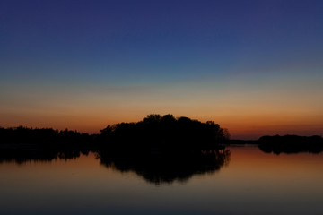 peaceful abstract landscape horizon silhouette of trees and island on a river water environment calm surface with reflection in long exposure photography at evening time