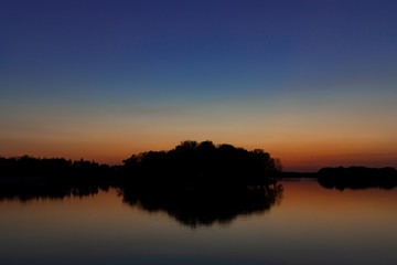 Naklejka premium peaceful abstract landscape horizon silhouette of trees and island on a river water environment calm surface with reflection in long exposure photography at evening time