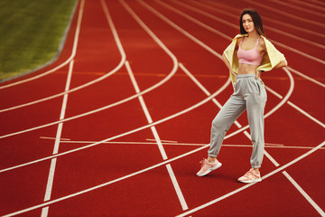 Obraz premium Beautiful young woman in sports wear looking at camera standing on the red stadium