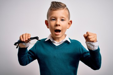 Young little caucasian kid holding eyesight glasses correction over isolated background screaming...