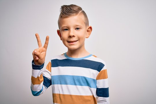 Young little caucasian kid with blue eyes standing wearing striped shirt over isolated background smiling with happy face winking at the camera doing victory sign. Number two.