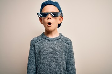 Young little caucasian kid wearing internet meme thug life glasses over isolated background afraid and shocked with surprise expression, fear and excited face.