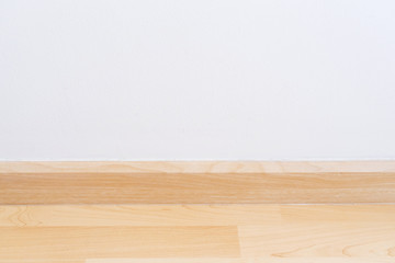 Wooden wall base skirting, finishing material with wood laminate floor and white mortar wall. Empty room with white wall and wooden floor.