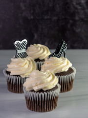 4 chocolate cupcakes with white frosting swirled high with a black and silver polka dot prom dress and high heel on top.