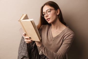 Photo of charming serious woman reading book and sitting on chair