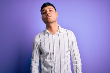 Young handsome hispanic man wearing elegant business shirt standing over purple background looking at the camera blowing a kiss on air being lovely and sexy. Love expression.