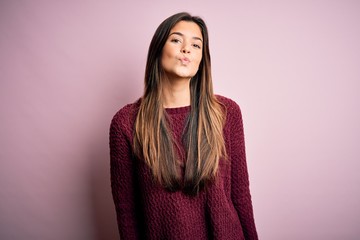 Fototapeta premium Young beautiful girl wearing casual sweater over isolated pink background looking at the camera blowing a kiss on air being lovely and sexy. Love expression.