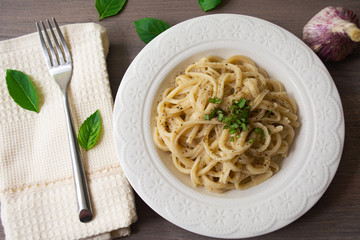 A vegan version of traditional Italian pasta fettuccine alfredo with creamy white sauce garnished with basil on a wooden surface with a fork, napkin, garlic and basil leaves