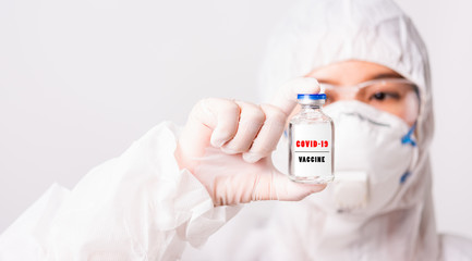 Asian female woman doctor or nurse in PPE uniform and gloves wearing face mask protective in laboratory holding medicine vial coronavirus vaccine bottle and on bottle has "COVID-19 VACCINE" text label