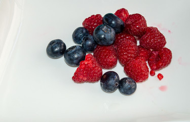 Red raspberries and blue blueberries in small heaps. White background.