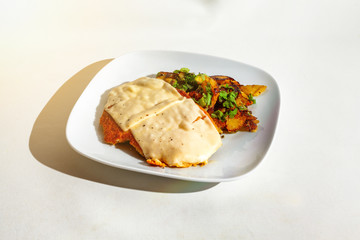 Schnitzel mit Käse überbacken mit Bratkartoffeln auf einen weißen Teller-Isoliert auf weiß
