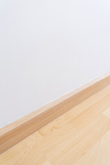 Wooden wall base skirting, finishing material with wood laminate floor and white mortar wall.