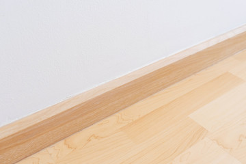 Wooden wall base skirting, finishing material with wood laminate floor and white mortar wall.
