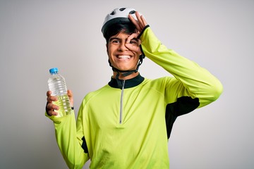 Young handsome cyclist man wearing security bike helmet drinking bottle of water with happy face smiling doing ok sign with hand on eye looking through fingers