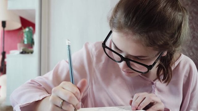 Face of serious teeanger in glasses with black frame drawing picture sitting at table.Close up view.