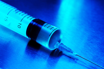 A single-use syringe lies on a metal table , a blue-tinged vaccine. Neon