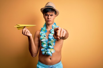 Young tourist man on vacation wearing swimwear and hawaiian lei flowers holding paper plane...