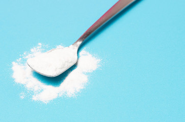 White collagen powder in teaspoon on a blue background, a copy of the space