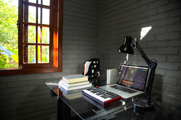 Home office desk with midi keyboard, notebook and books. Window with garden in the background.