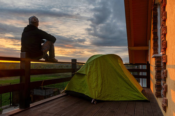 Wanderlust at the coronavirus quarantine. Man sitting by the tent admires the sunset from the terrace.
