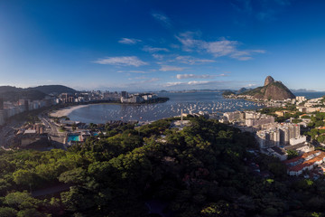 Botafogo beach and Sugarloaf mountain on either side of Guanabara bay port for pleasure boats against a blue sky with the Pasmado hill park and viewpoint in the foreground