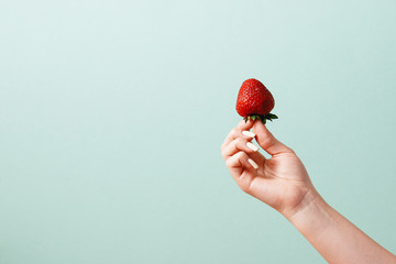 Woman holds strawberry in hand on front of grey-blue background