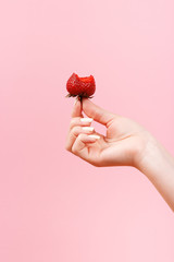 A woman holds a bitten strawberry in her hand on a light green background