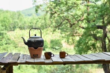 Black kettle with tea cup on old wooden battens with natural green background