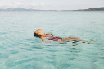 Portrait of young woman enjoying and relaxing in clean transparent ocean water. Leisure, carefree and vacation concept. Wanderlust travel in Asia.
