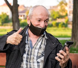 Happy senior man in facial mask using a smartphone