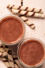 Two glasses of hot chocolate. Cocoa with marshmallow. Waffle tubes. Light background. Coffee with cream