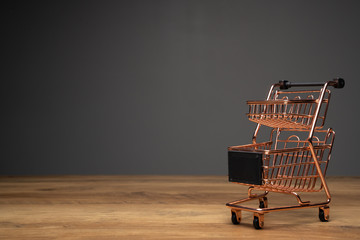 Small empty shopping cart or metal trolley in copper colour on top of wooden top and dark...