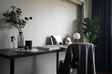 Bedroom working corner decorated with laptop, white candles and artificial plant in glass vase on black wood  working table with beige painted wall in the background /apartment interior / copy space