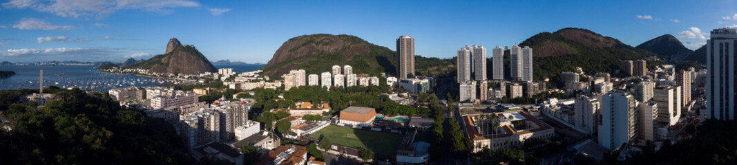 Super wide panorama of Botafogo and Urca neighbourhoods in Rio de Janeiro with high rise buildings and mountains such as the Sugarloaf mountain against a clear blue sky