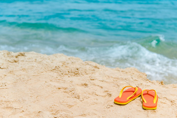 Orange flip flops or slippers on tropical island beach. Footwear for summer holiday or relaxing vacation. Summertime travel concept