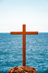 wood cross on cliff in front of large blue sea